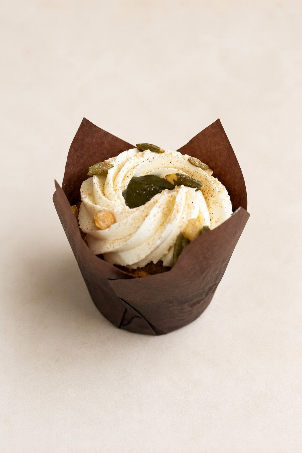 Muffin Marchew z kardamonem Batida - muffinka w brązowej papilotce, z kremem i pestkami dyni