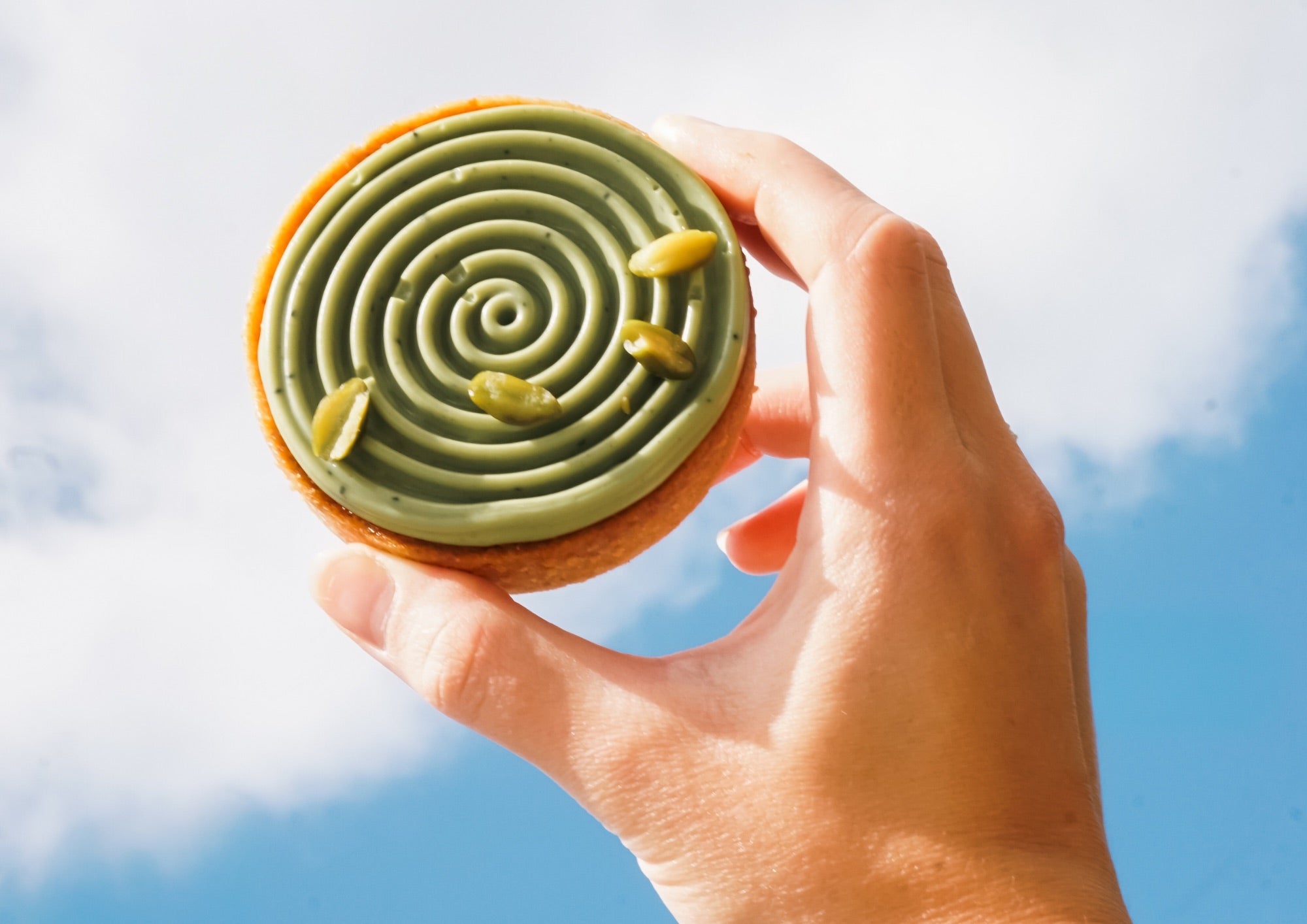 Tartaletka matcha Batida trzymana w dłoni na tle nieba