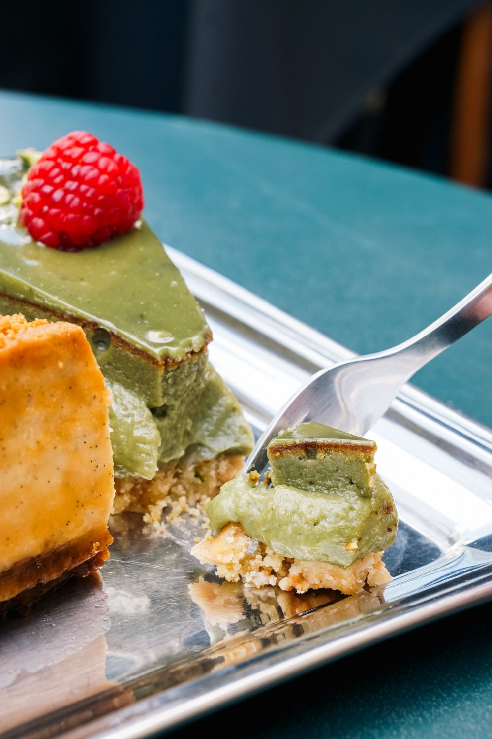 Matcha-Batida-Käsekuchen mit Himbeeren und Pistazien, ein Stück auf einer Gabel