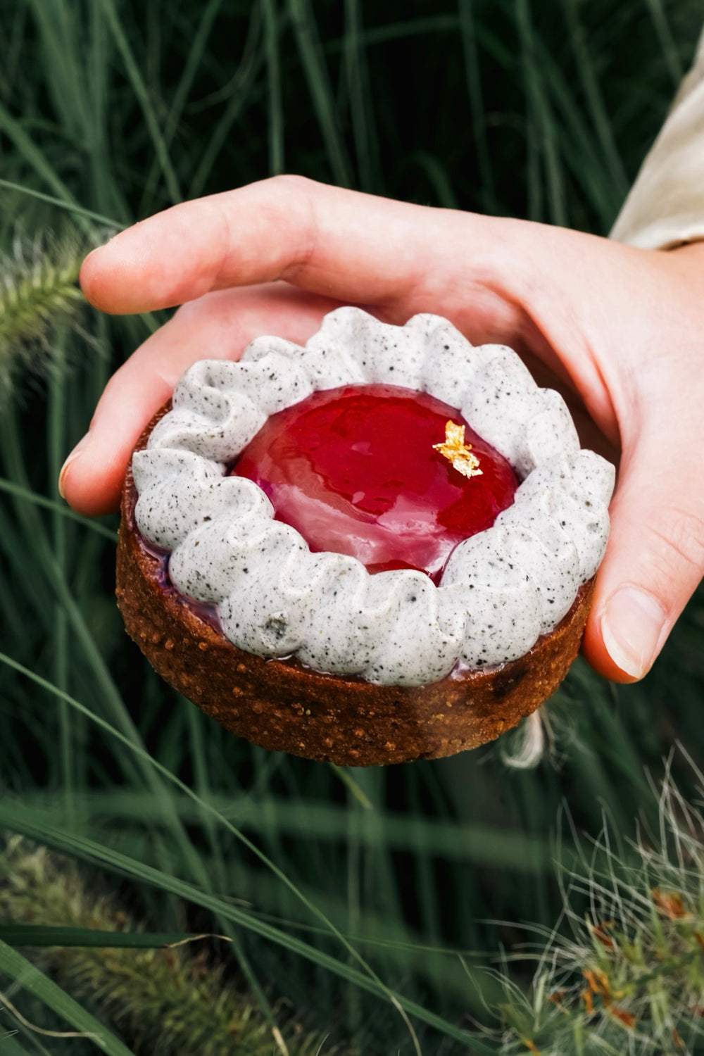 Schwarze-Sesam-Tartelette Batida mit Kirschkonfitüre in den Händen, im Hintergrund Gräser