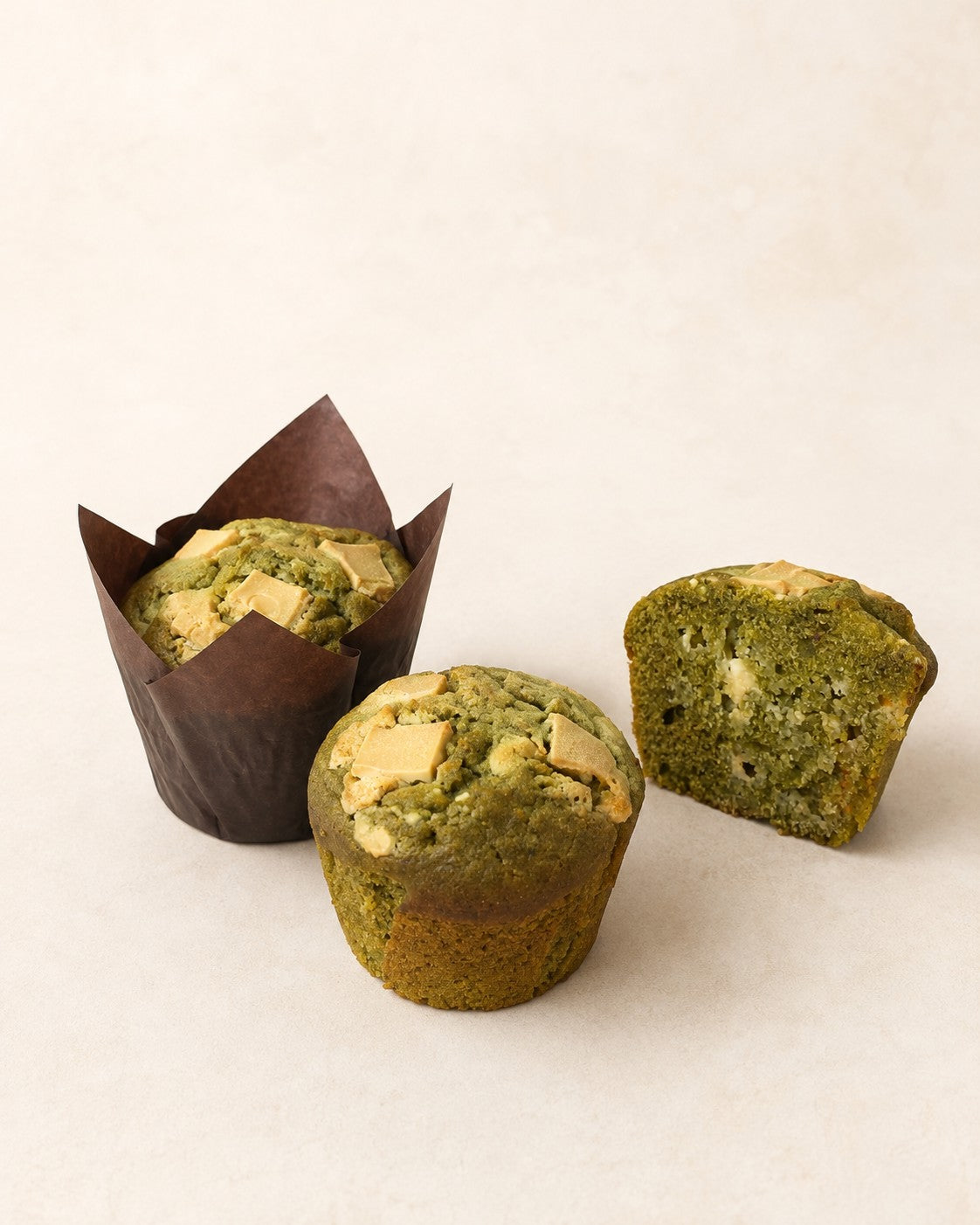 Muffin Matcha z białą czekoladą Batida - dwie muffinki, w papilotce i bez, oraz połówka z widocznym przekrojem