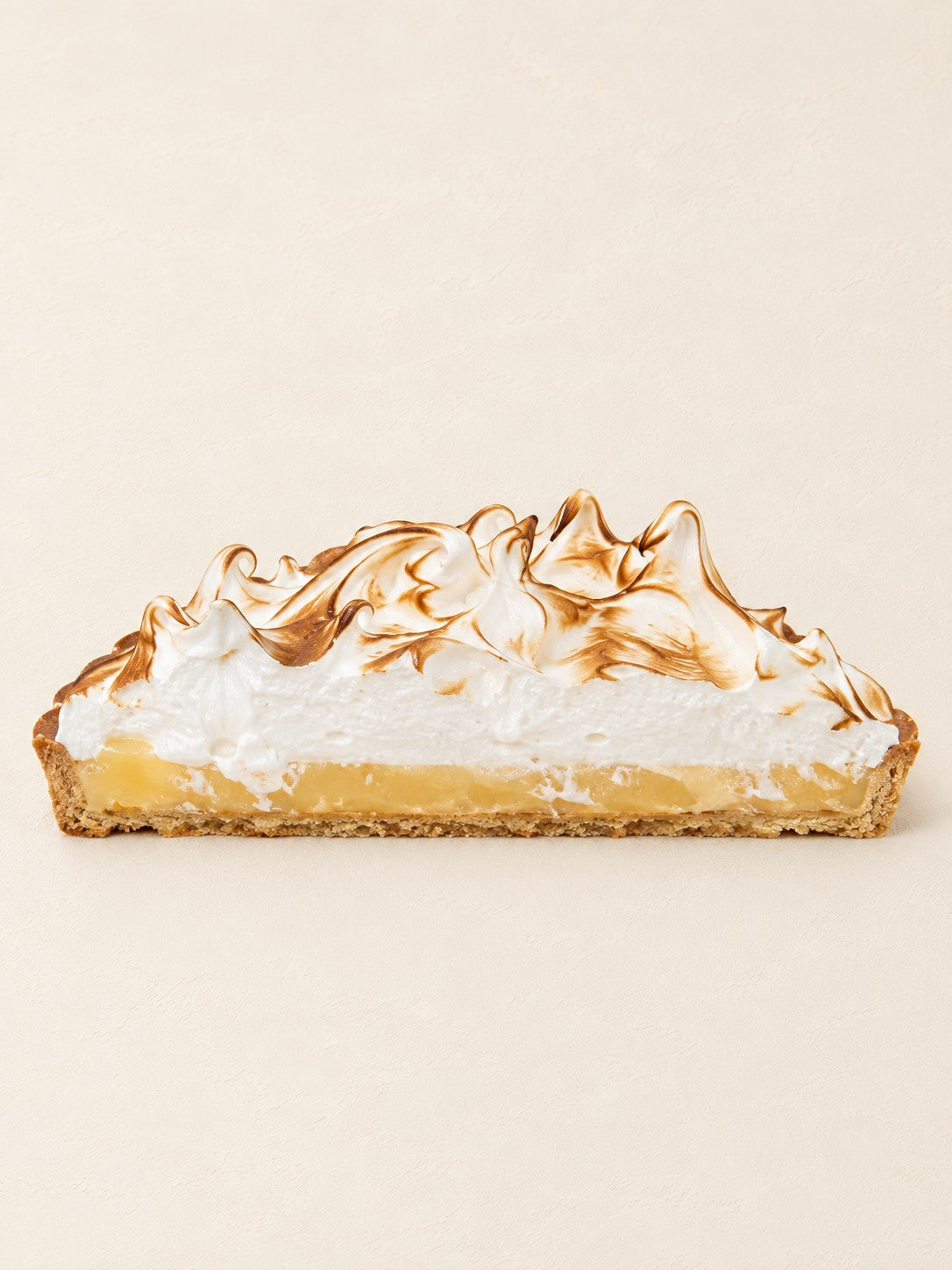Tarta cytryna - yuzu z opalaną bezą Batida - połówka tarty z boku, widać kruchy spód, curd i bezę